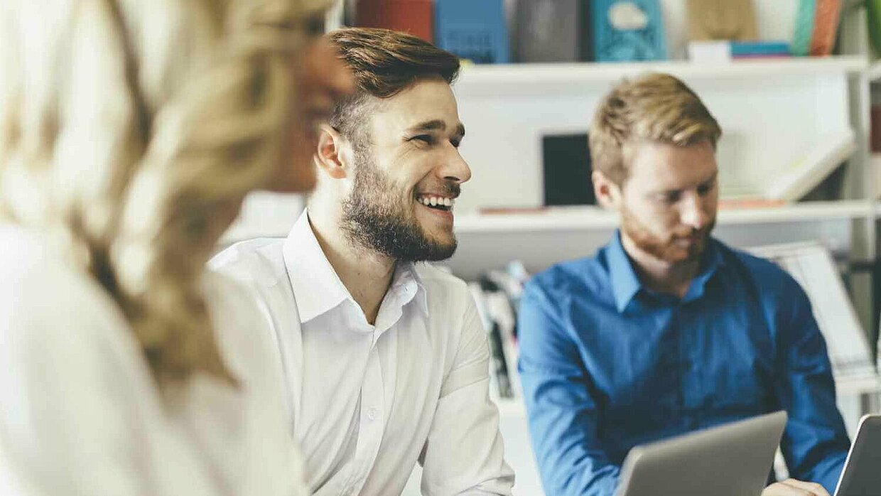 Qualifizierung Fachkräfte Gruppe von Studierenden sitzt vor einem Laptop und lacht.