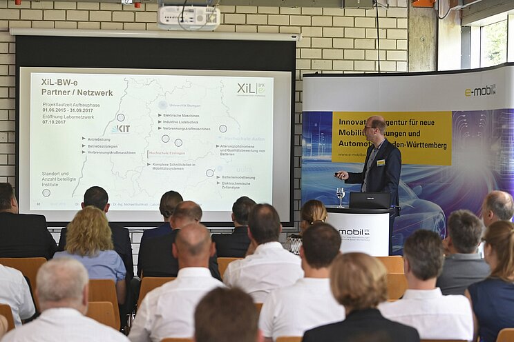 Mitarbeiter der e-mobil BW hält einen Vortrag. Das Publikum hört ihm gespannt zu.
