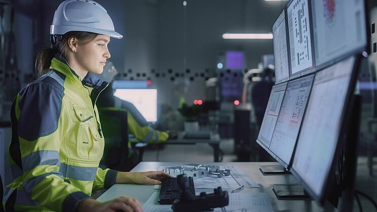 Industry 4.0 Modern Factory: Female Facility Operator Controls Workshop Production Line, Uses Computer with Screens Showing Complex UI of Machine Operation Processes, Controllers, Machinery Blueprints