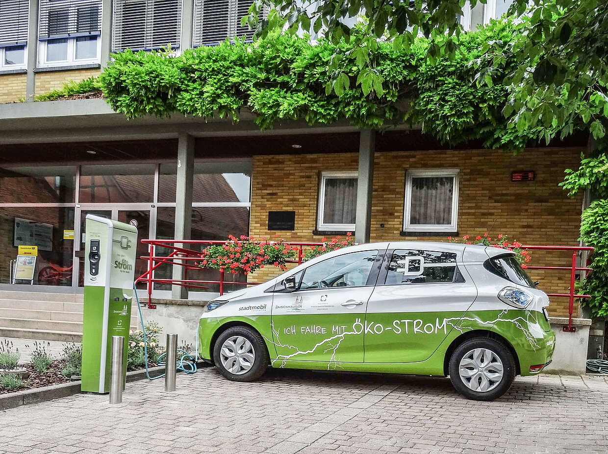 Stadtmobil Carsharing Ein Fahrzeug, das mit Ökostrom fährt wird an einer Ladestation geladen. Im Hintergrund ist ein Gebäude zu sehen.