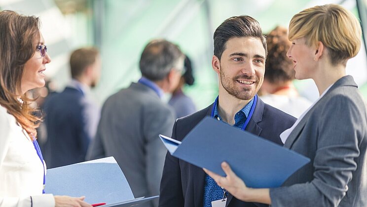 Zwei Frauen und ein Mann in Business Klamotten unterhalten sich auf einer Veranstaltung.