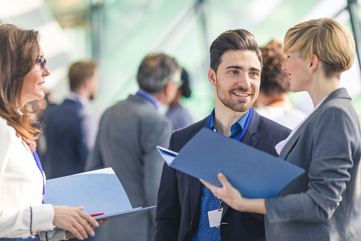 Zwei Frauen und ein Mann in Business Klamotten unterhalten sich auf einer Veranstaltung.