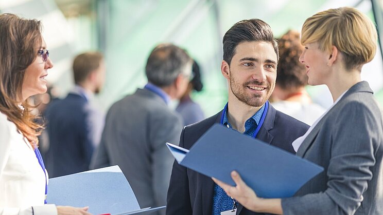 Zwei Frauen und ein Mann in Business Klamotten unterhalten sich auf einer Veranstaltung.