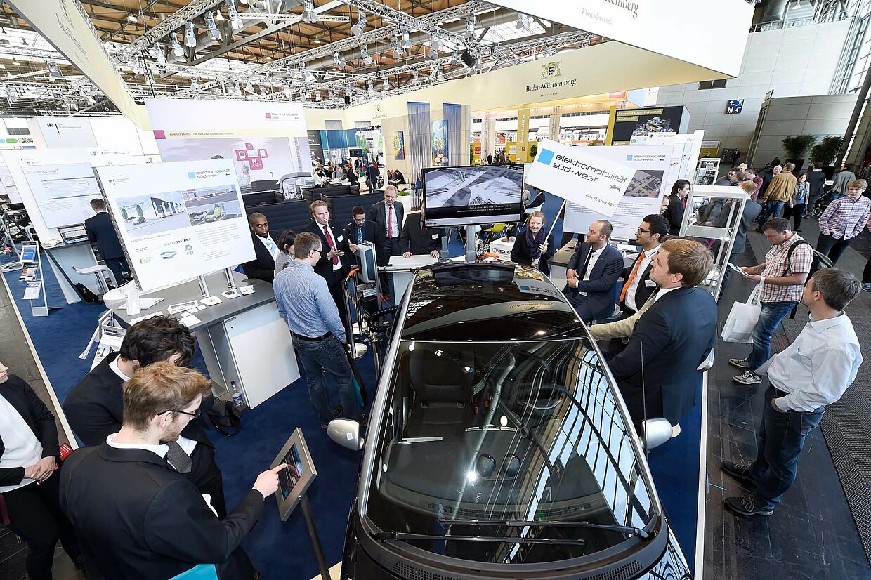 Menschen auf einer Veranstaltung stehen an verschiedenen Ständen.