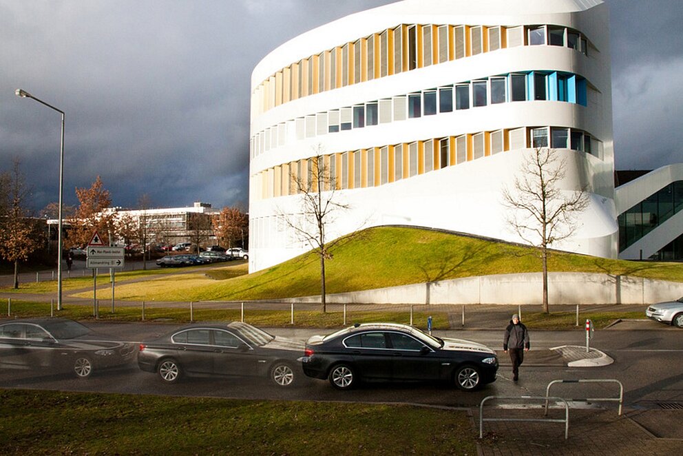 Weißes Gebäude des Fraunhofer IAO wird von der Sonne angestrahlt, auf der Straße davor parken Autos.