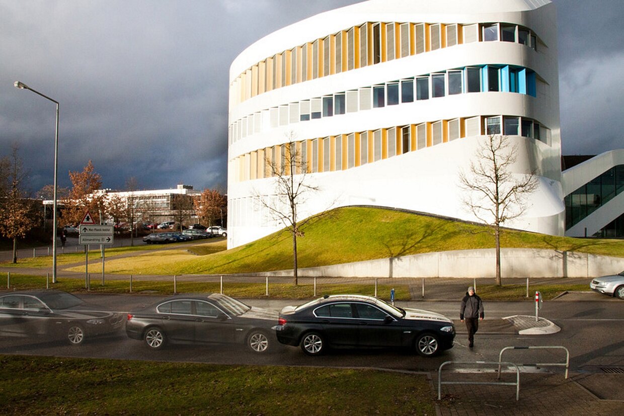 Weißes Gebäude des Fraunhofer IAO wird von der Sonne angestrahlt, auf der Straße davor parken Autos.